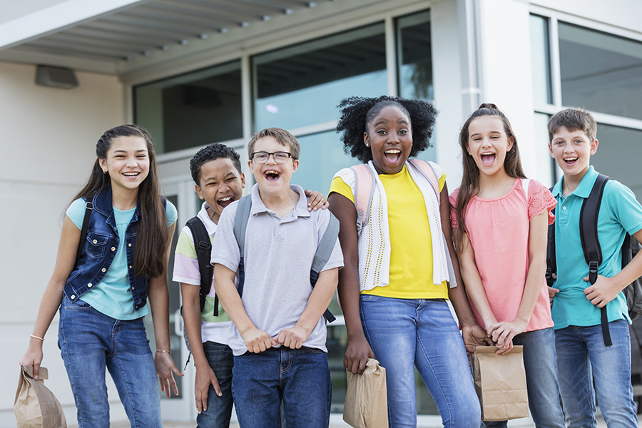 Group of 6 kids laughing and dressed for school with their backpacks and lunches.