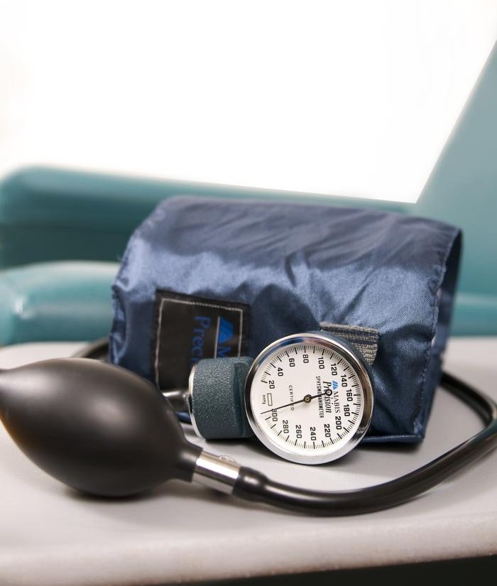 Manual blood pressure cuff on a side table next to a teal armchair.