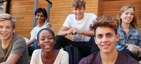 Group of six teenagers sitting on steps, smiling, and looking at the camera.